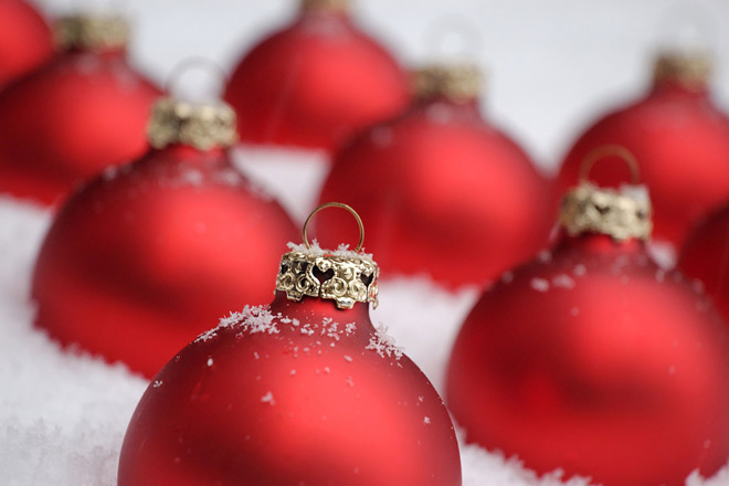Wir wünschen frohe Feiertage Rote Christbaumkugeln im Schnee.