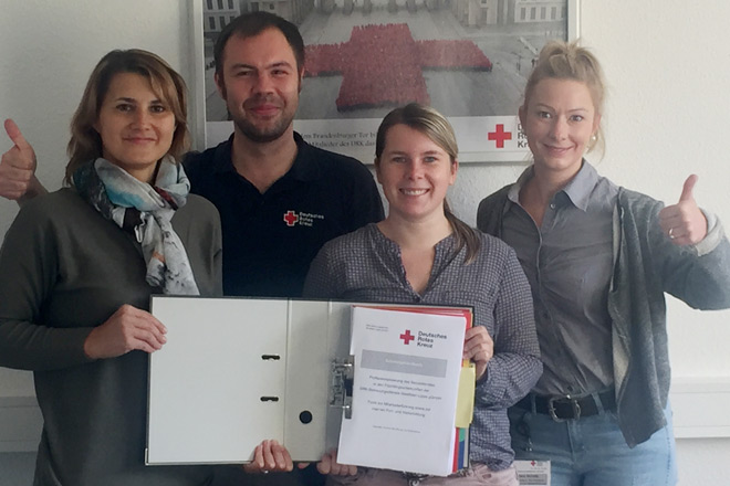 Neues Fortbildungskonzept für unsere Mitarbeiter Drei Frauen und ein Mann halten das Schulungshandbuch in die Kamera und machen die Geste "Daumen hoch".
