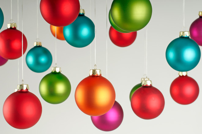 Frohe Weihnachten und einen guten Rutsch! Bunte Christbaumkugeln hängen vor einem grauen Hintergrund.