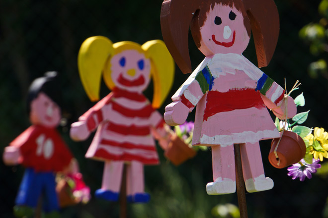 Ein buntes Frühlingsfest für Kinder Drei bunt bemalte Holzfiguren, die Kinder in Sommerkleidung darstellen.