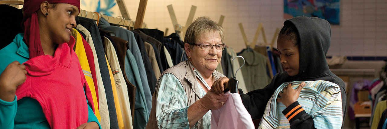 Ehrenamtliche Helferin berät zwei Frauen in der Kleiderkammer