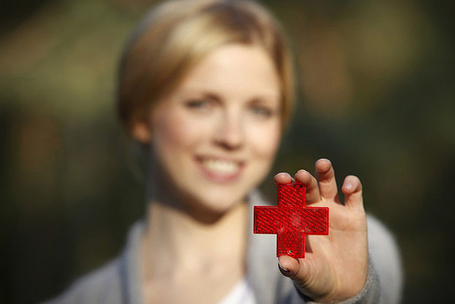 Junge blonde Frau hält ein rotes Kreuz in die Kamera