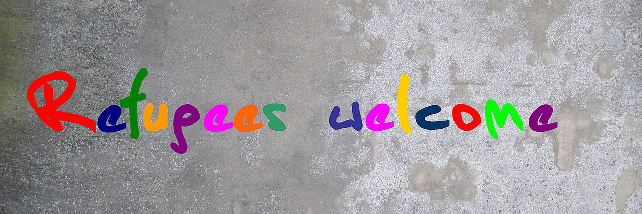 Schriftzug "Refugees welcome" in bunten Buchstaben auf grauem Grund.